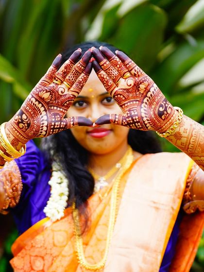 A creative pose by a bride, forming a triangle with her hands to showcase her intricate back-hand mehendi design.