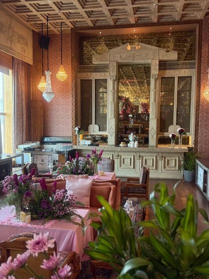 A wider view of the Mehendi lounge area, where pink tablecloths and floral centerpieces continue the romantic theme. The setting is both luxurious and comfortable, inviting guests to relax and celebrate.