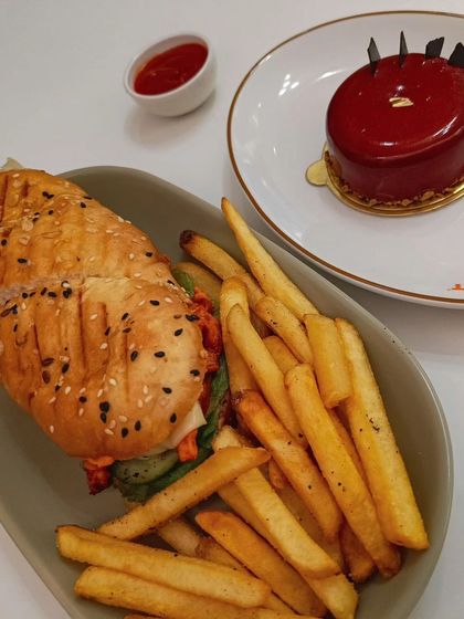 A customer's meal featuring a peri-peri chicken sandwich, fries, and our glossy red Cherry and Chocolate pastry. It shows how you can enjoy both a savory meal and a gourmet dessert at my café.