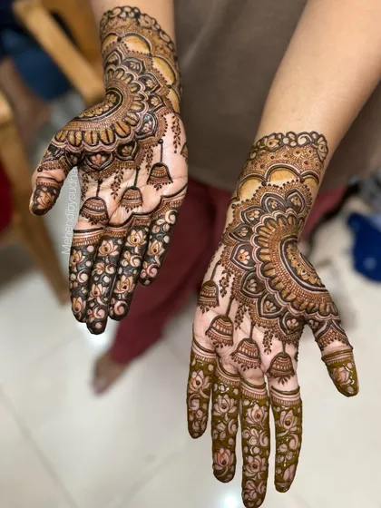 This angle highlights the hanging jhumka motifs on the palm, a playful and traditional element in bridal mehendi. The design is filled with delicate lotus flowers and fine line work.
