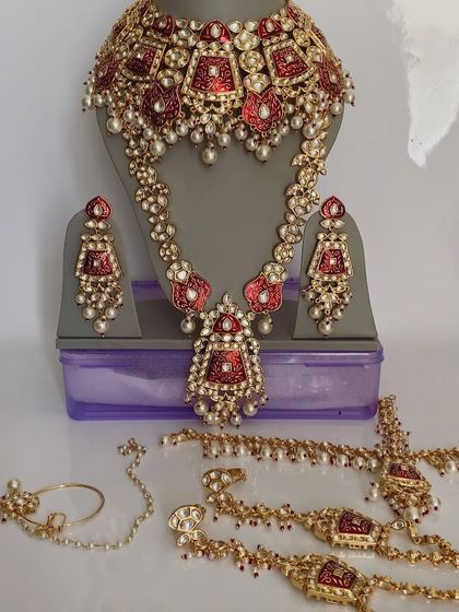 A full bridal set with red meenakari work and pearl detailing. This set comes with a choker, long necklace, earrings, nath, maang tikka, and hathphool, providing everything a bride needs.