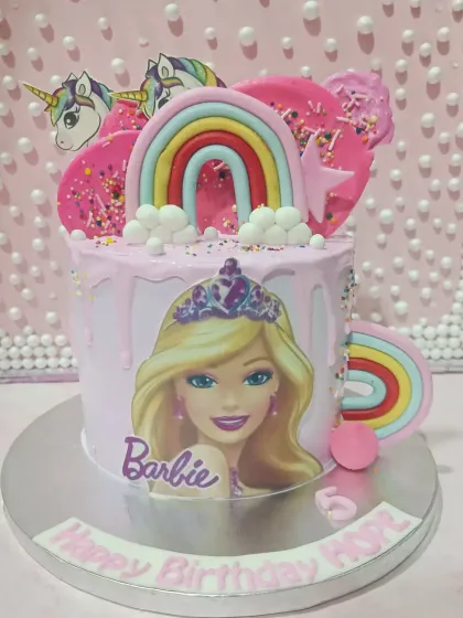 A fun and colorful Barbie-themed drip cake. This pink cake is decorated with rainbows, unicorns, and a Barbie illustration for a magical celebration.