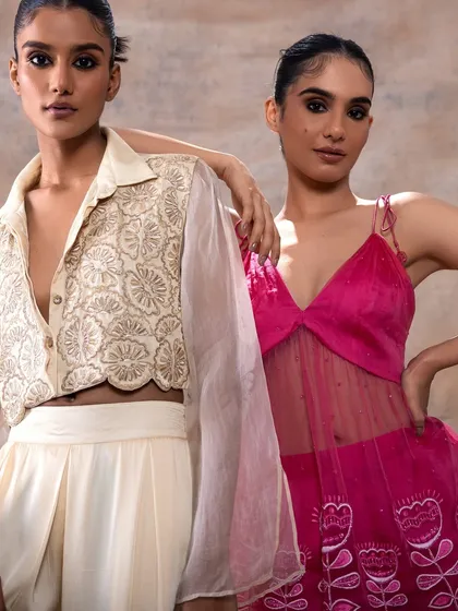 A portrait of two models in complementary outfits. The makeup is consistent and polished across both, with a focus on a strong eye look that ties their individual styles together.