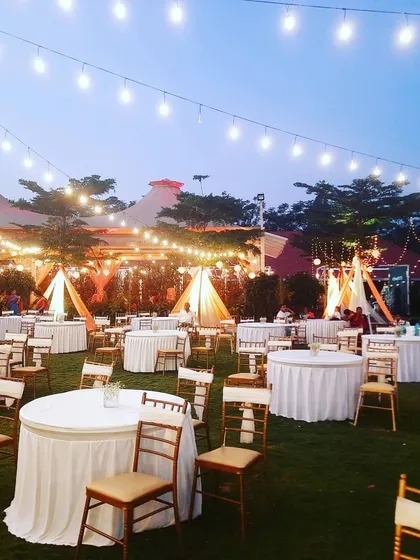 I create the perfect ambiance for evening events, like this outdoor reception setup with string lights casting a warm glow over the lawn. The seating arrangement with classic round tables and white linens provides an elegant and inviting atmosphere for guests.