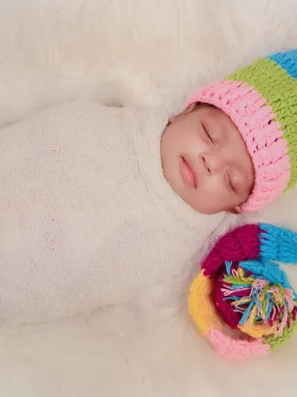 A cozy, swaddled newborn wearing a colorful, long rainbow-striped hat. This simple setup on a white fur rug makes the colors pop.