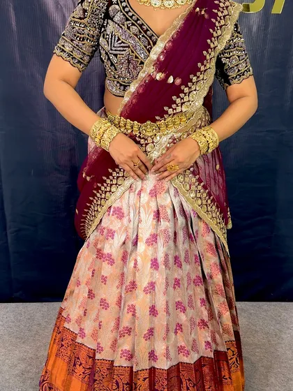 A full view of the South Indian half saree. You can see the neat pleats of the skirt and the way the dupatta is securely draped over the shoulder and around the waist.