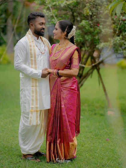 A classic portrait of the couple holding hands in a lush garden. Their traditional attire looks stunning against the natural green backdrop.