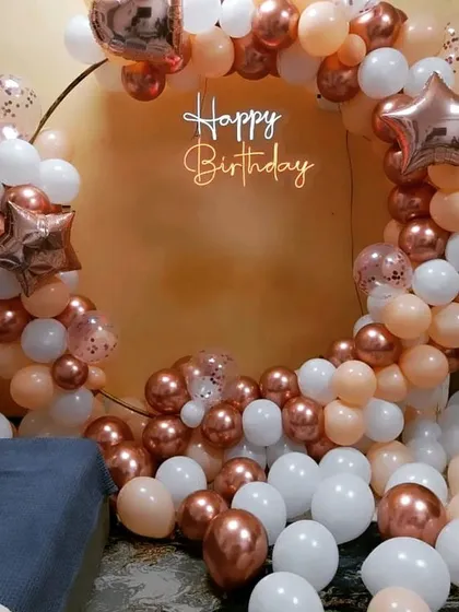 A beautiful rose gold, peach, and white balloon ring with a "Happy Birthday" neon sign, perfect for an intimate home party.