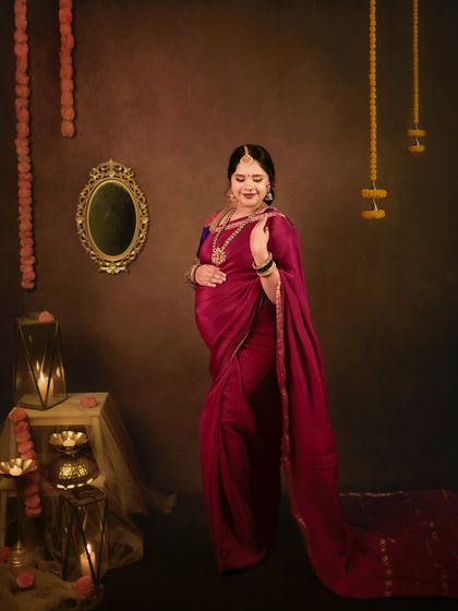 The flowing trail of the magenta saree adds a touch of grace and movement to this beautiful traditional maternity photo.