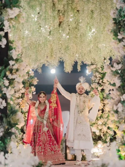 A joyous moment of celebration under a cascade of flowers, as the couple raises their hands in happiness after the ceremony.