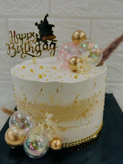 A dreamy white and gold cake decorated with iridescent "bubble" spheres and a whimsical witch topper, perfect for a magical birthday.