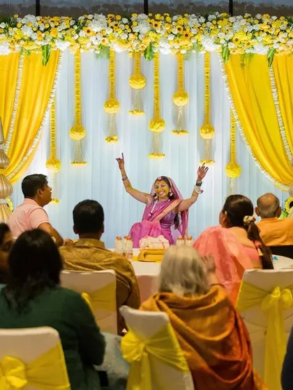 The bride takes center stage, celebrating with her guests during her haldi ceremony, set against a bright yellow backdrop.