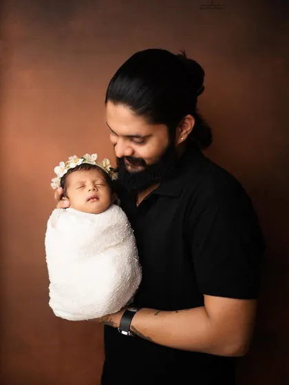 A proud father holds his swaddled newborn, looking down with a gentle smile. This portrait perfectly captures the special bond between a dad and his new baby.
