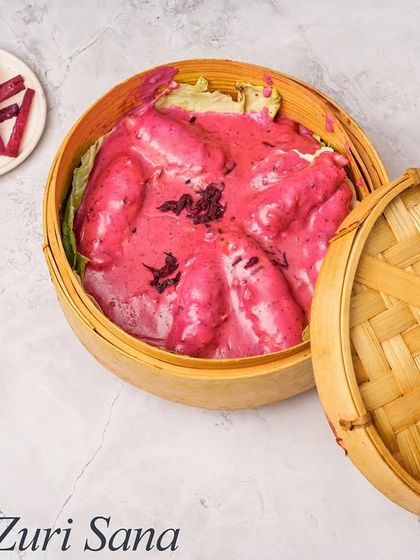 The Zuri Sana Chicken is a unique chef's special. It's served in a traditional bamboo steamer basket and features chicken in a vibrant pink, creamy sauce.