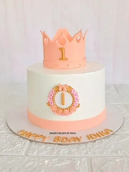 A simple and elegant crown cake in peach and white for a royal first birthday celebration.