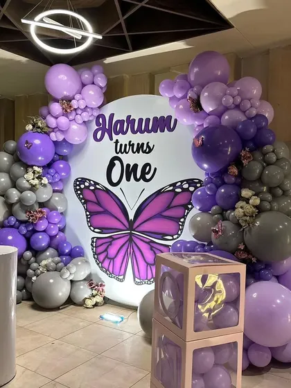 Another angle of the butterfly party decor, showing the arrangement of purple and grey balloons and the transparent "ONE" blocks.