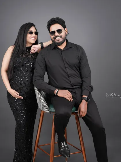A fun and stylish couple portrait in matching black outfits and sunglasses. Their playful energy and coordinated look create a cool and modern maternity photo.