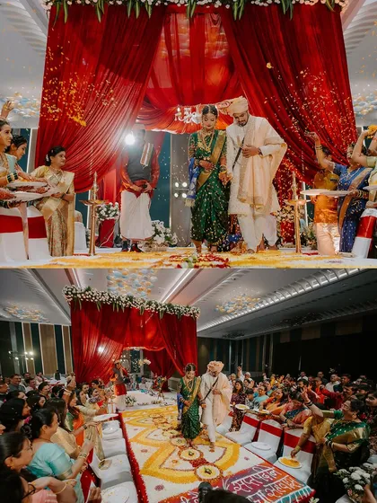 The grand scale of an indoor Maharashtrian wedding ceremony, with a stunning red backdrop and guests showering the couple with blessings and petals.