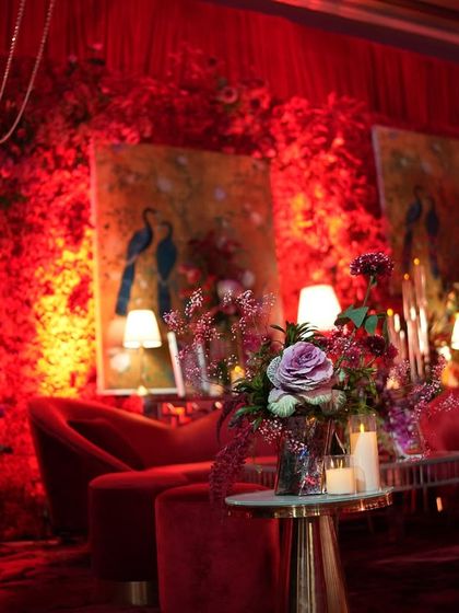 Another view of the red-on-red lounge, highlighting the rich textures of the floral walls and the elegant seating. Floor lamps and table lamps cast a soft, intimate glow, making the bold space feel warm and inviting.