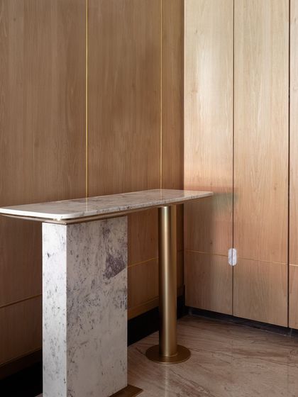 A minimalist console table that makes a powerful statement. We combined a thick marble slab with a single, sculptural brass leg, set against a backdrop of warm wood paneling.