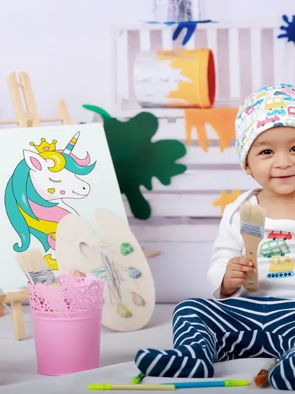 Welcome to the art studio. This little Picasso, holding a paintbrush, is surrounded by easels and colorful paint splatters in our artist-themed shoot.