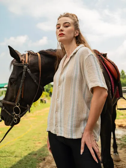 Another angle from the same fashion shoot, showing the model and horse in a relaxed pose. The natural greenery and open sky provide a clean and appealing backdrop.