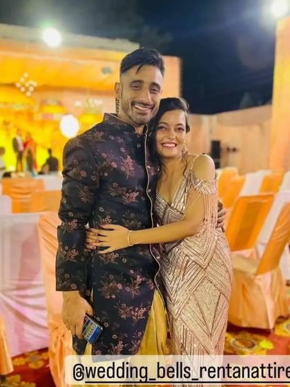 A happy couple at a sangeet or cocktail night. The groom is wearing a dark floral print Indo-Western jacket, a stylish and modern choice.