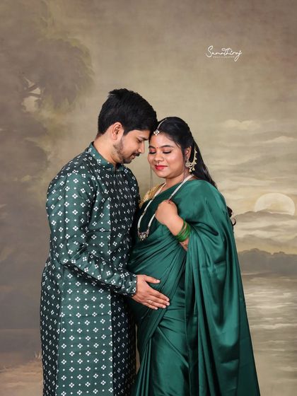 An intimate portrait of a couple sharing a quiet moment. The rich green saree and traditional printed kurta complement each other perfectly against the artistic backdrop, telling a story of love and anticipation.