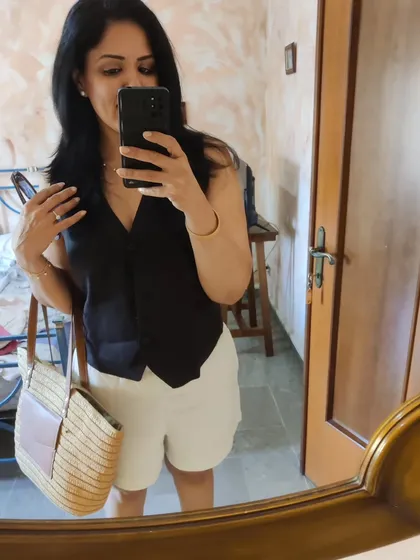 A mirror selfie showing my comfortable travel look: beige linen shorts and a black waistcoat.