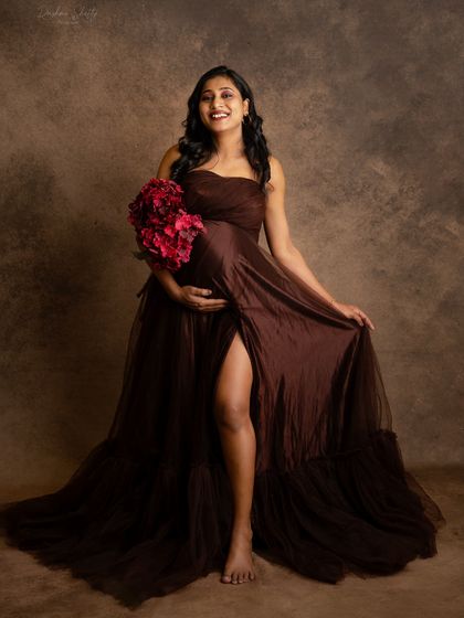 A simple, elegant pose holding a bouquet of flowers. The rich brown of the gown complements the studio backdrop perfectly, creating a warm and classic portrait.