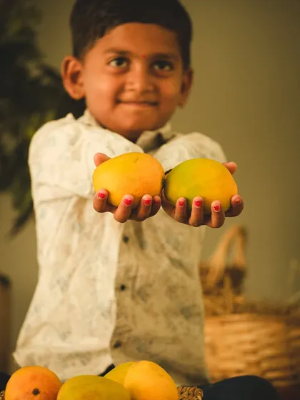 A young boy proudly presents two ripe mangoes. This image connects the product with a sense of pride and happiness, creating a positive emotional link for the brand.