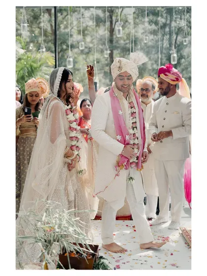 A candid shot of the couple during their pheras. The groom's happy expression and the guests in the background create a lively and joyful ceremony photograph.
