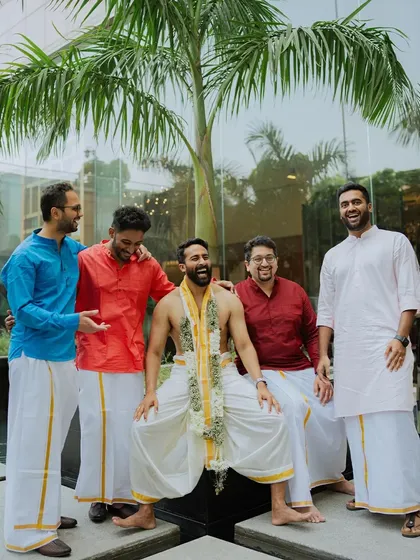 The groom shares a laugh with his groomsmen, all dressed in traditional South Indian attire.