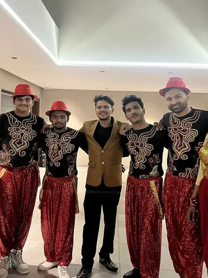 Our team of male and female dancers in vibrant red and yellow folk-inspired costumes, posing with our lead choreographer backstage before a performance.