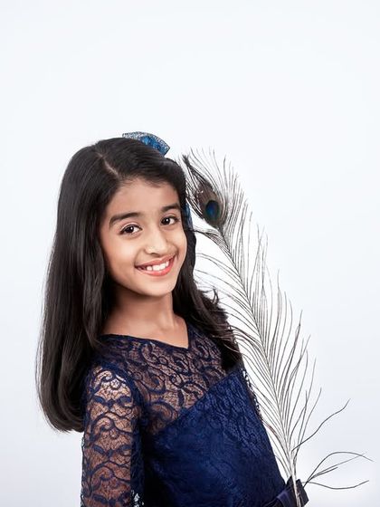 A simple and elegant studio portrait. The addition of a single peacock feather as a prop adds a unique and artistic touch to this young girl's photo.