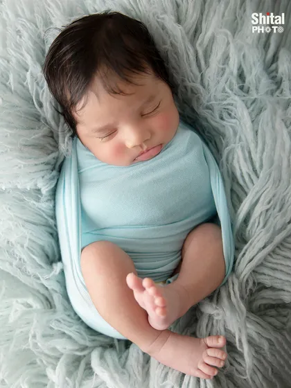 A close-up of a newborn swaddled in a light blue wrap on a soft, textured blanket, showcasing their tiny, perfect feet.