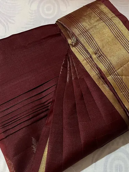 A deep maroon saree with a simple gold border, elegantly folded.