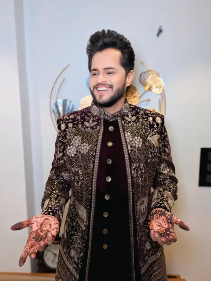 A joyful groom showing off his mehndi. The rich color of his outfit and the intricate details are complemented by a glowing, happy face.