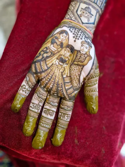 The fresh henna paste shows the intricacy of the family portrait. The names of the bride's 'aai-baba', 'didi', and 'masi' are clearly written on her fingers.