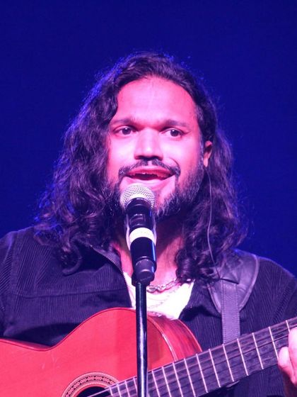 A close-up of Nikhil Paul George singing and playing guitar.