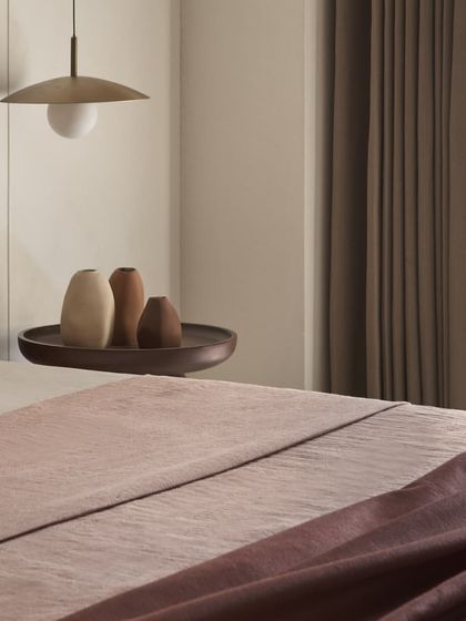 A close-up of the bedside details in the dusty rose room, showing the earthy linen bedding and minimalist ceramic vases. These textures and tones contribute to the room's calming atmosphere.