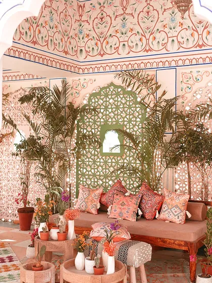 A beautiful lounge area set against intricately patterned walls at The Leela Palace. The decor combines lush plants, bohemian cushions, and traditional architecture for a stunning effect.