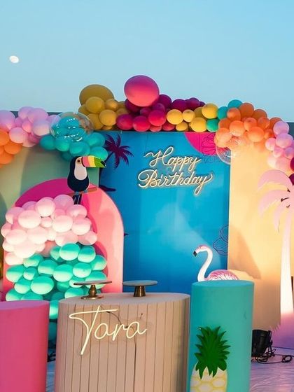 This is a duplicate of ID 15. This vibrant tropical flamingo theme is perfect for a fun and colorful celebration. The setup includes custom-arched backdrops, a multi-colored organic balloon arch, themed props like flamingos and toucans, and a personalized cake stand.