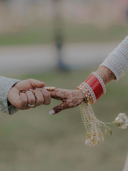 A close up shot of the couple holding hands, focusing on the bride's red chooda and intricate henna design.