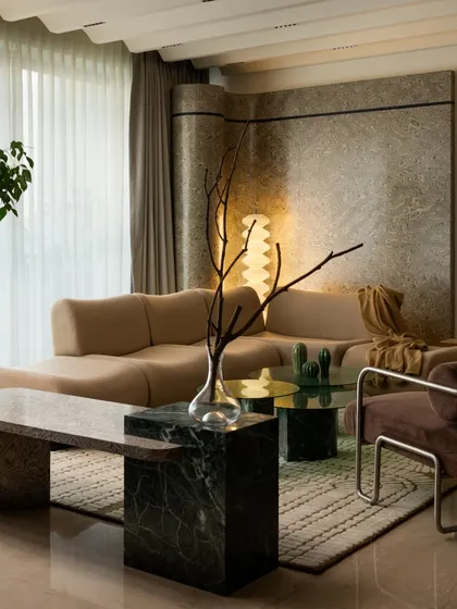 The living area is designed for comfort and conversation. The large, custom-made bouclé sofa is paired with a marble bench and a unique green glass coffee table, all resting on a bespoke rug that ties the space together.
