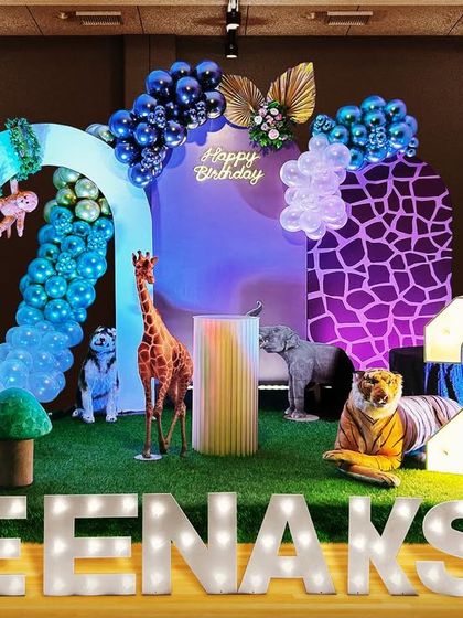 A design concept for a modern jungle theme. This setup for Meenakshi uses stylish arch backdrops with a giraffe-print pattern, deep blue chrome balloons, and a mix of animal props for a unique look.