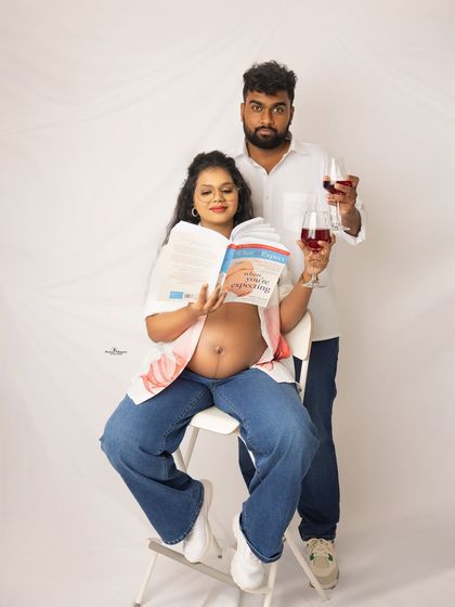 A humorous and relatable shot of a couple reading a pregnancy book while enjoying a glass of non-alcoholic wine. It's all about capturing your real-life moments.