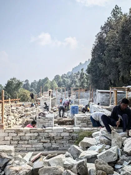 A wide view of the bustling construction site in Uttarakhand, where multiple teams of artisans work on stacking stones for the walls of the guesthouses. The entire process is a symphony of coordinated manual labor.