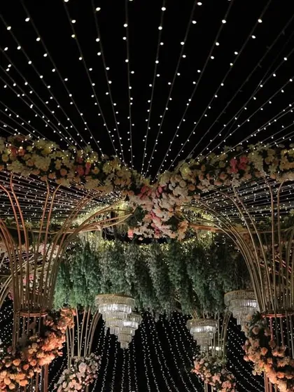 As day turns to night, the magic truly comes alive. This grand floral mandap, transformed under a canopy of thousands of twinkling fairy lights, creates an enchanting and romantic atmosphere for an evening wedding ceremony.