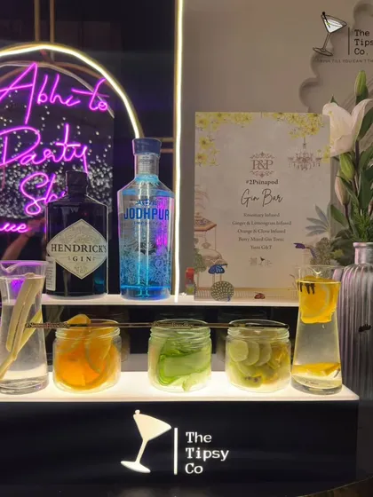 A personalized Gin Bar for a wedding reception. The setup includes premium gins like Hendrick's and Jodhpur, fresh botanicals in glass jars, and a neon sign that reads 'Abhi to Party Shuru Hui Hai'.
